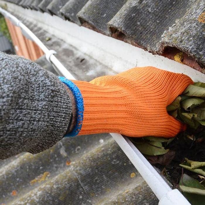 Hand met werkhandschoen in een dakgoot